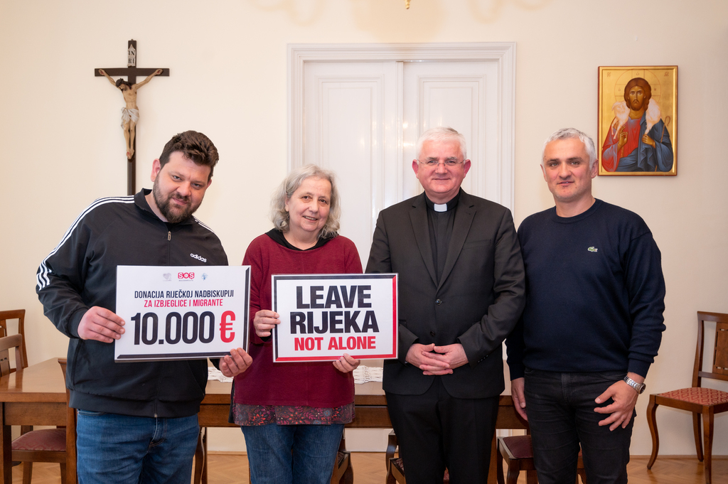 Gruppenfoto von vier Menschen, darunter der Erzbischof, Petar Rosadić und Roswitha Feige. Die letzteren halten Schilder hoch auf denen steht: "10.000€" und "LEAVE RIJEKA NOT ALONE"