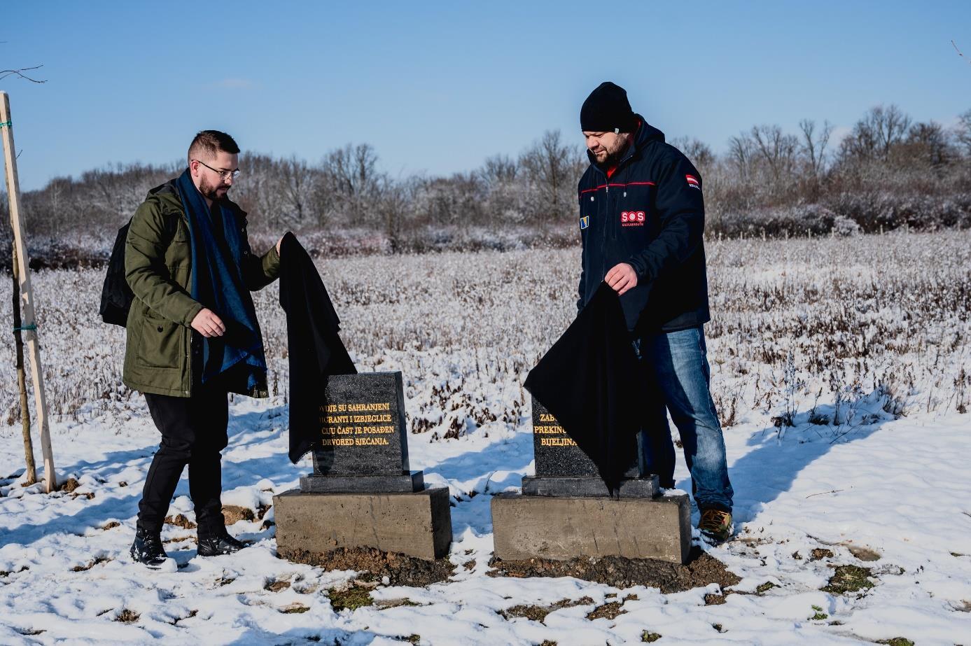 Zwei schwarze Grabsteine werden von zwei Männern enthüllt. Es liegt Schnee.